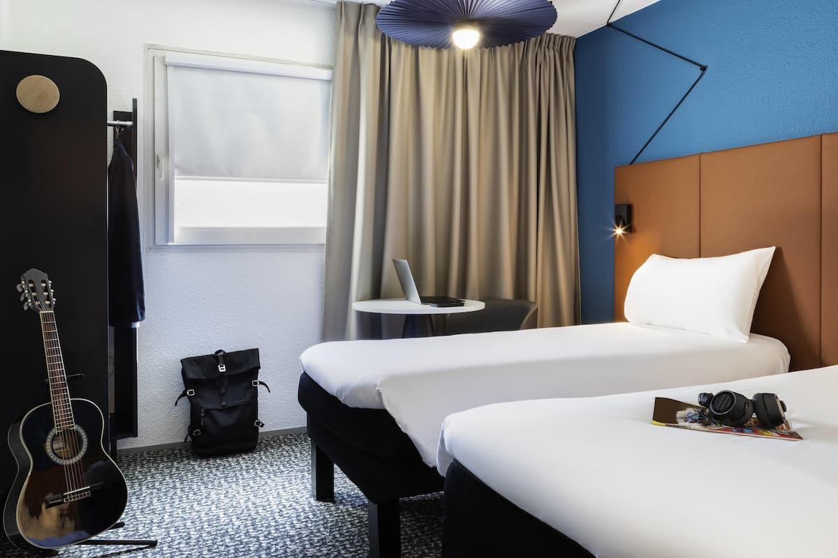 Habitación de hotel con dos camas, una guitarra, una mesita y un ventilador de techo.