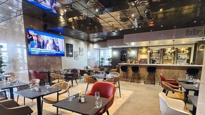 A restaurant with multiple tables and chairs, a bar area, and a television screen displaying a news program.