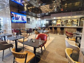 A restaurant with multiple tables and chairs, a bar area, and a television screen displaying a news program. - ibis Paris Porte De Bercy (Charenton-le-Pont)