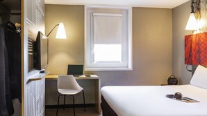 Et hotelværelse med en seng, et skrivebord med en bærbar computer, en stol, et klædeskab og et vindue med rullegardiner.