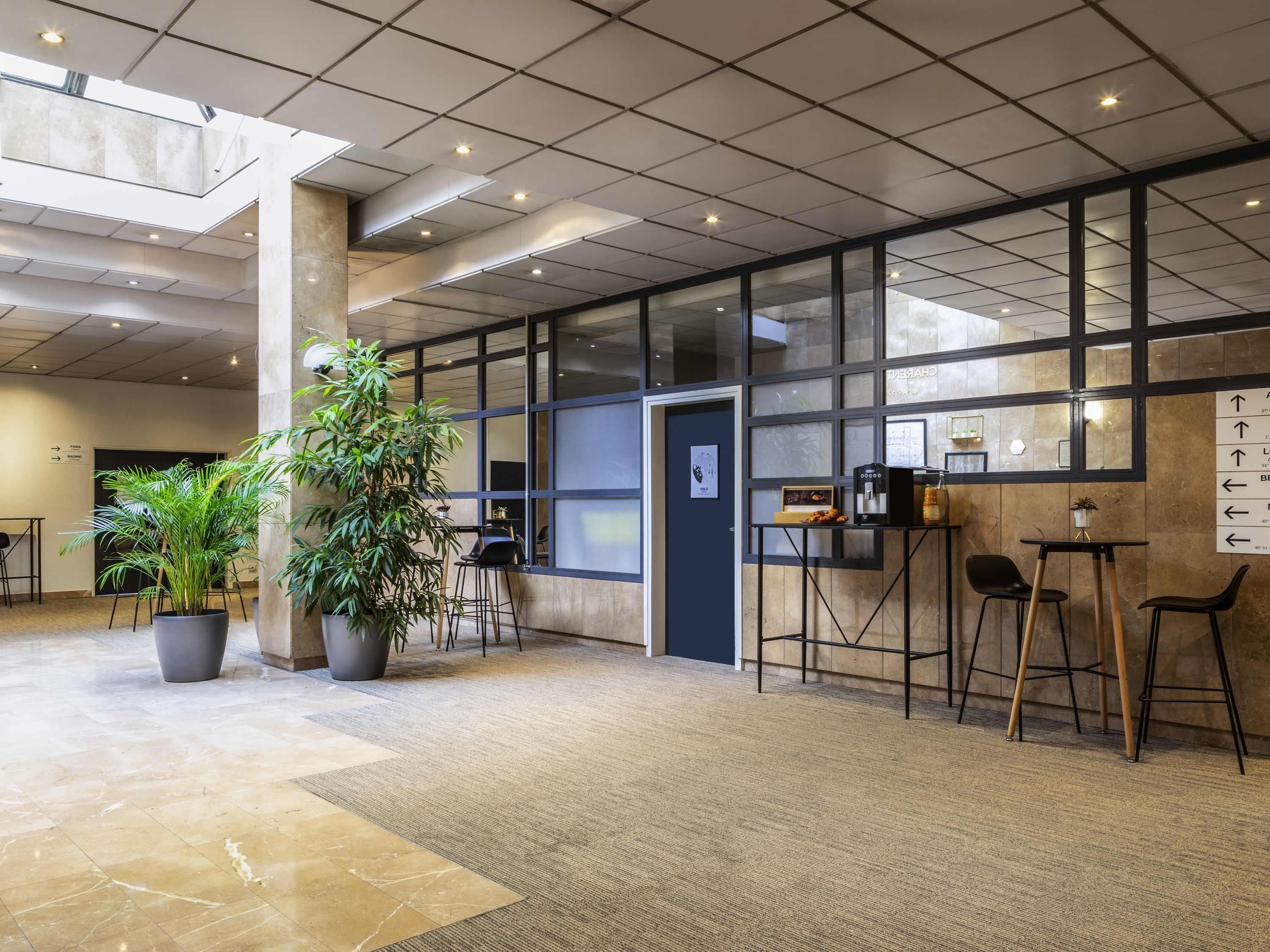 A modern lobby with a high ceiling, large windows, and a seating area with tables and chairs.