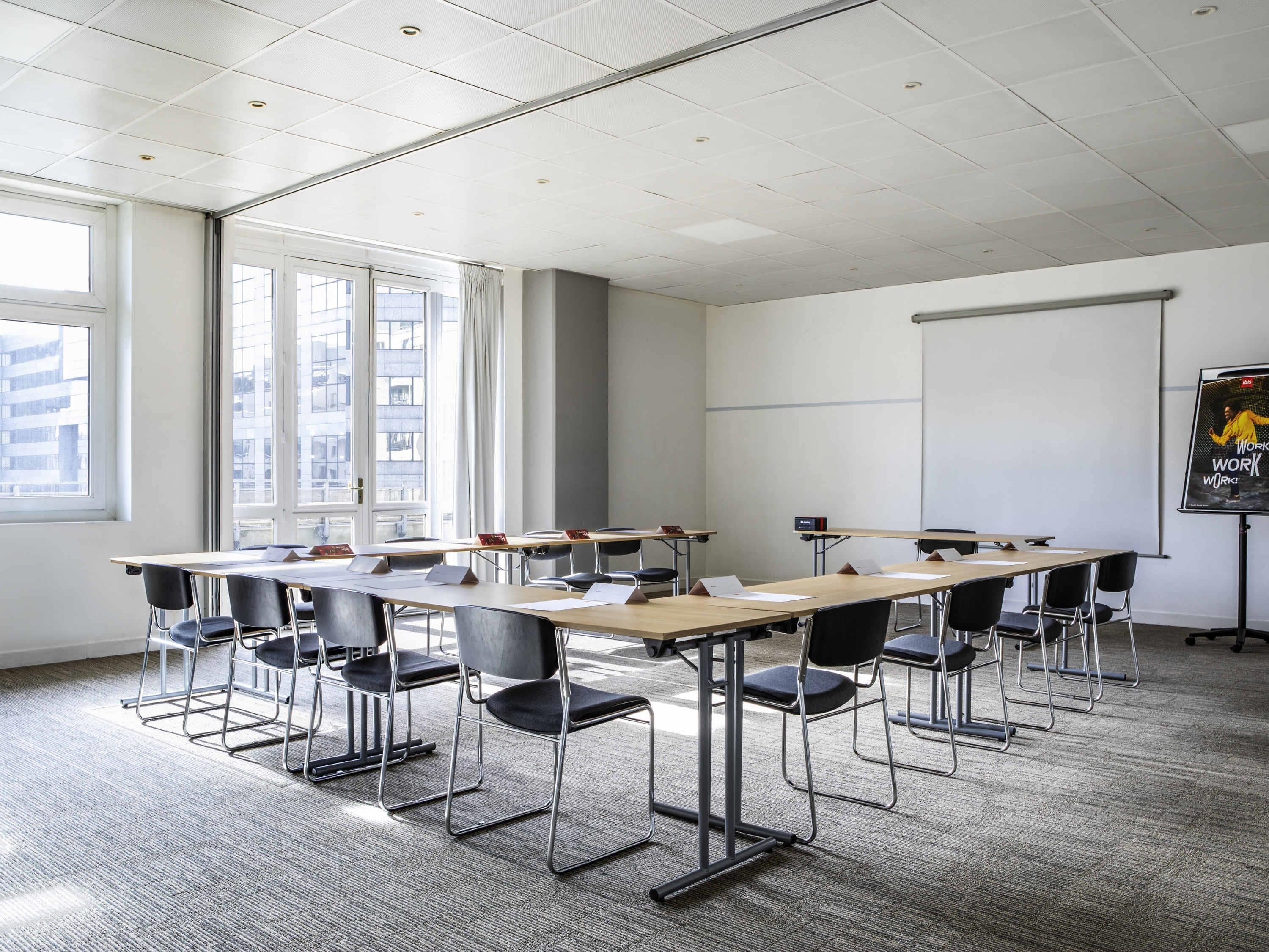 Ett konferensrum med ett långt bord, stolar, en projektorduk och stora fönster.