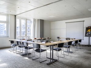 Un salón de conferencias con una larga mesa, sillas, una pantalla de proyector y ventanas amplias.