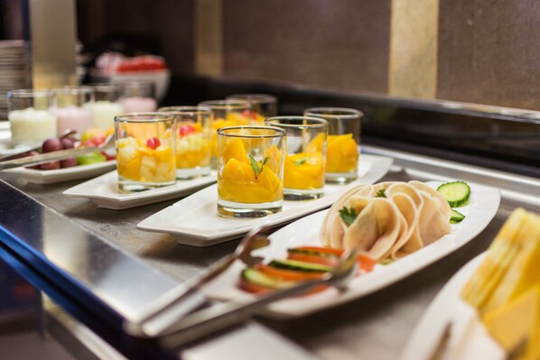Una mesa de buffet con diversos platos, incluyendo copas de fruta, dumplings y un plato con verduras.