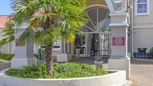 Entrada de hotel com uma palmeira em primeiro plano, céu claro e uma placa com a inscrição 'Mercure Hotel'.