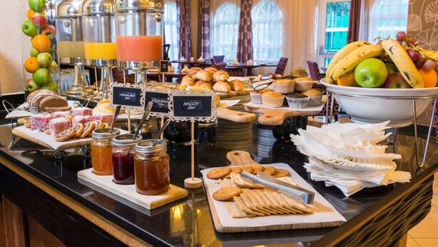 Buffet com diversos alimentos e bebidas, incluindo frutas, doces e acompanhamentos.