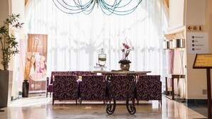 Um saguão com um candelabro, uma mesa de recepção e uma placa indicando as comodidades.