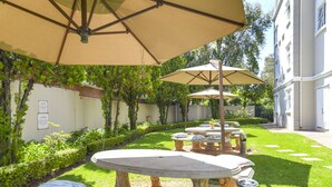 A courtyard with outdoor seating under umbrellas, surrounded by greenery and a building. - Mercure Johannesburg Randburg Hotel (Randburg)