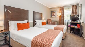 Quarto de hotel com duas camas, uma escrivaninha, uma televisão e uma cadeira.