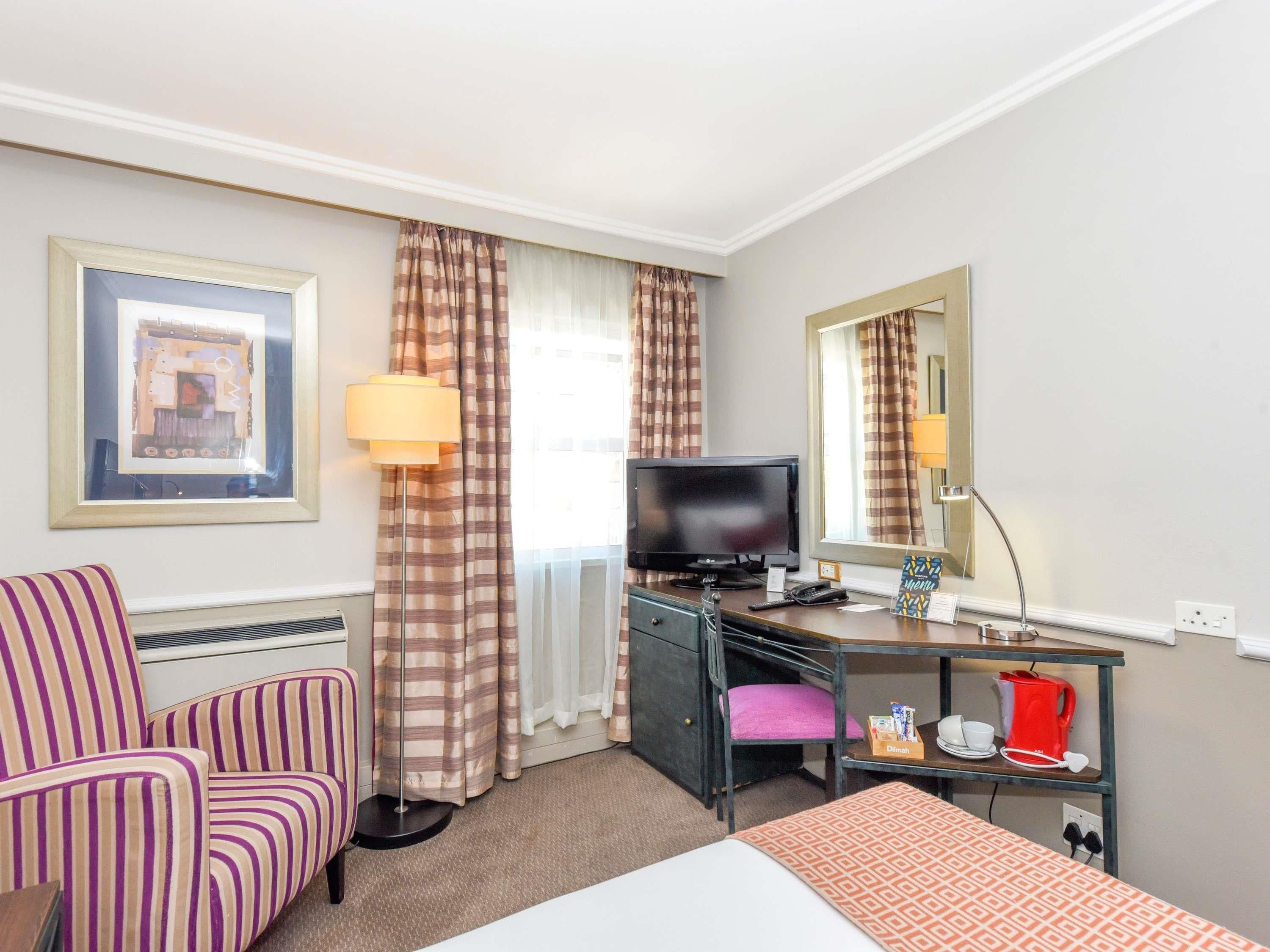 A hotel room with a bed, a desk with a computer, a chair, a television, and a mirror.