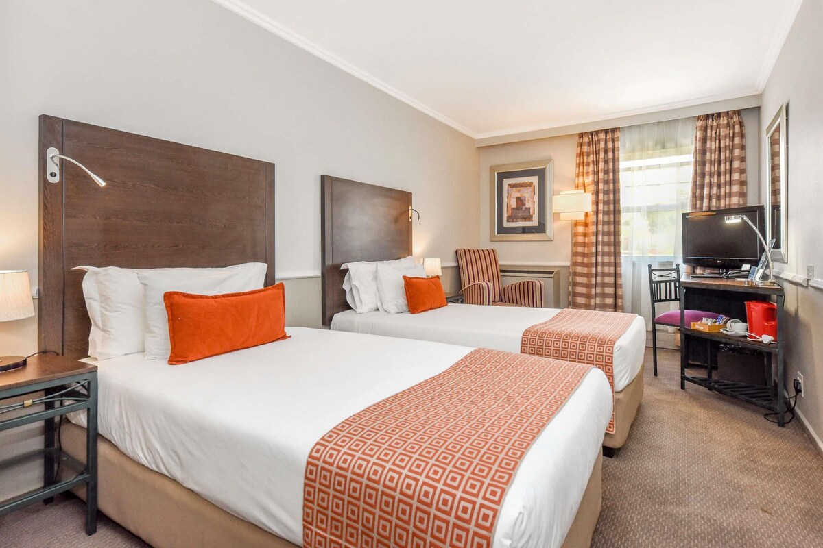 A hotel room with two beds, a desk, a television, and a chair.