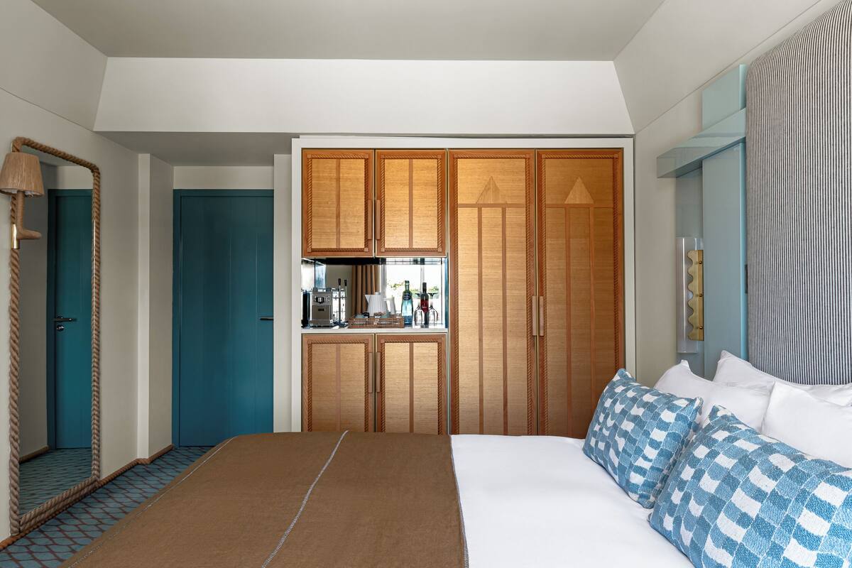 A hotel room with a bed, a desk with a coffee machine, a wardrobe, and a mirror.