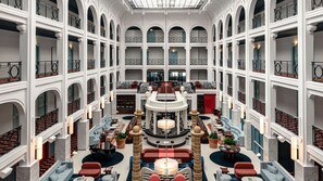 A multi-level hotel lobby with a central seating area, multiple balconies, and a high ceiling with skylights. - Regina Experimental Biarritz (Biarritz)