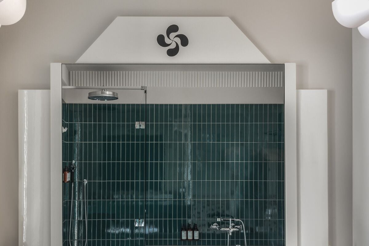 A modern bathroom with a glass shower enclosure, a visible logo on the wall, and a towel rack.