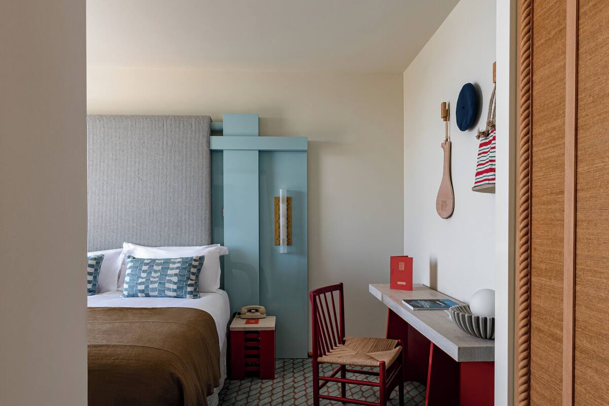 A compact hotel room with a bed, a small desk, a chair, and a wardrobe.