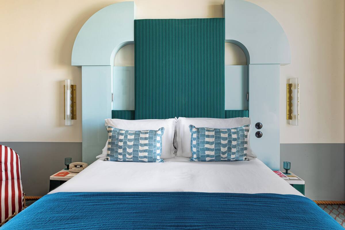 A hotel room with a large bed, two pillows, a nightstand, a telephone, and a chair.