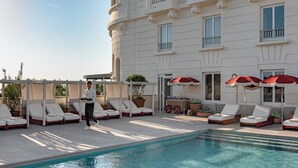 A poolside area with lounge chairs and umbrellas, a waiter walking, and a building with balconies. - Regina Experimental Biarritz (Biarritz)