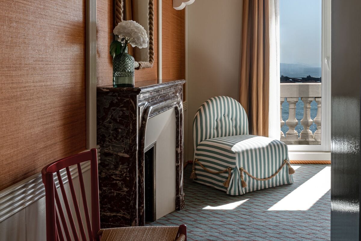 A room with a fireplace, a striped armchair, and a view of the sea.