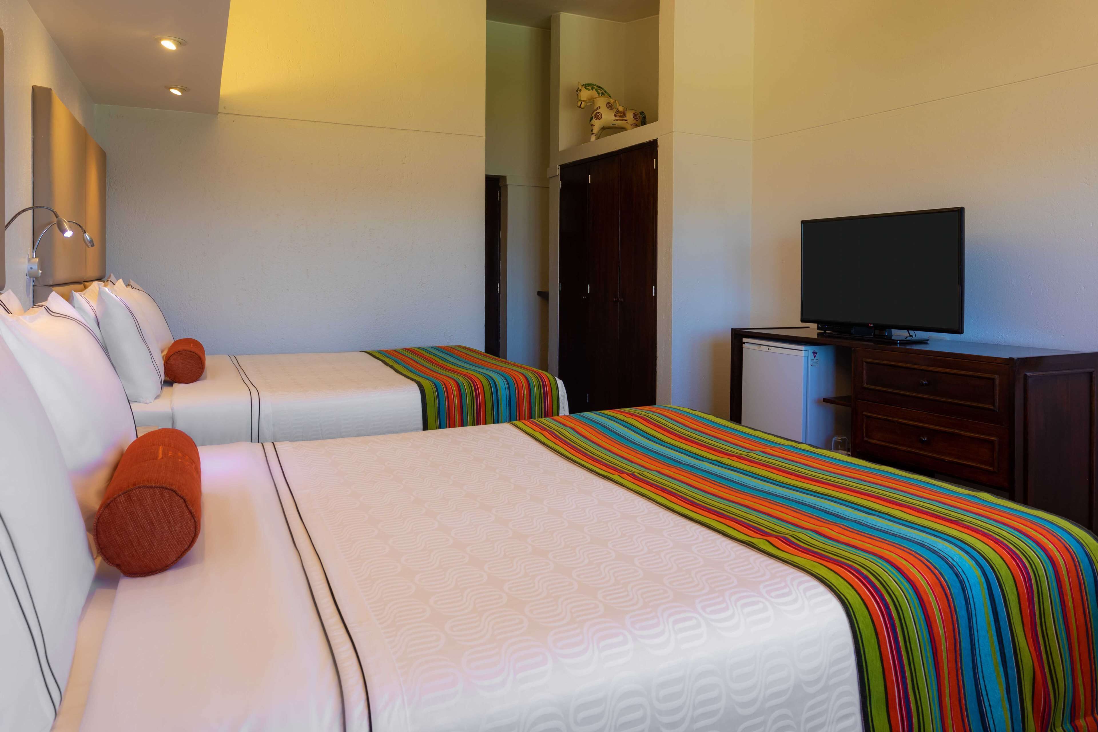 A hotel room with two beds, a television, a dresser, and a door with a horse decoration.