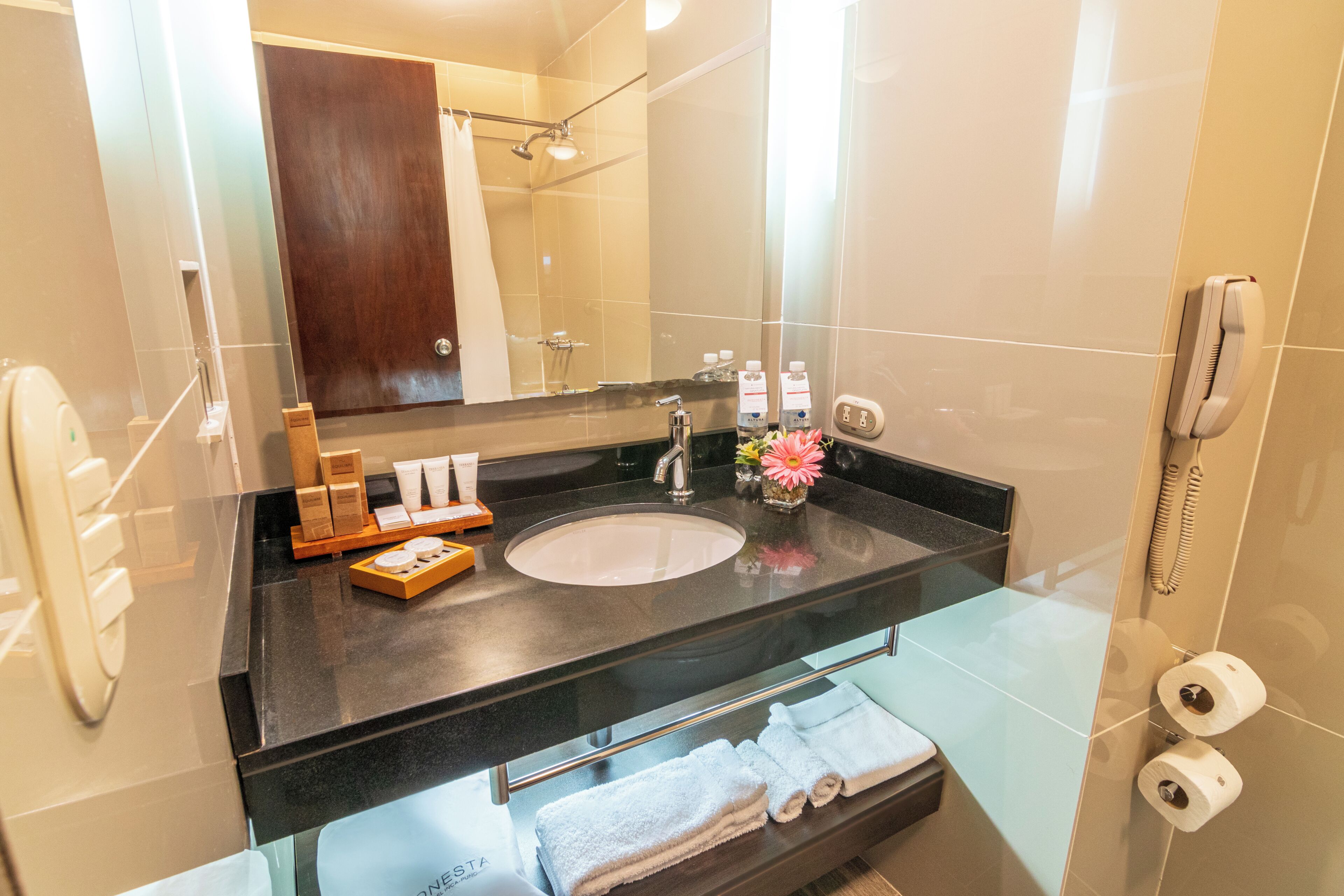 A modern bathroom with a large mirror, a sink, a shower, and a telephone.