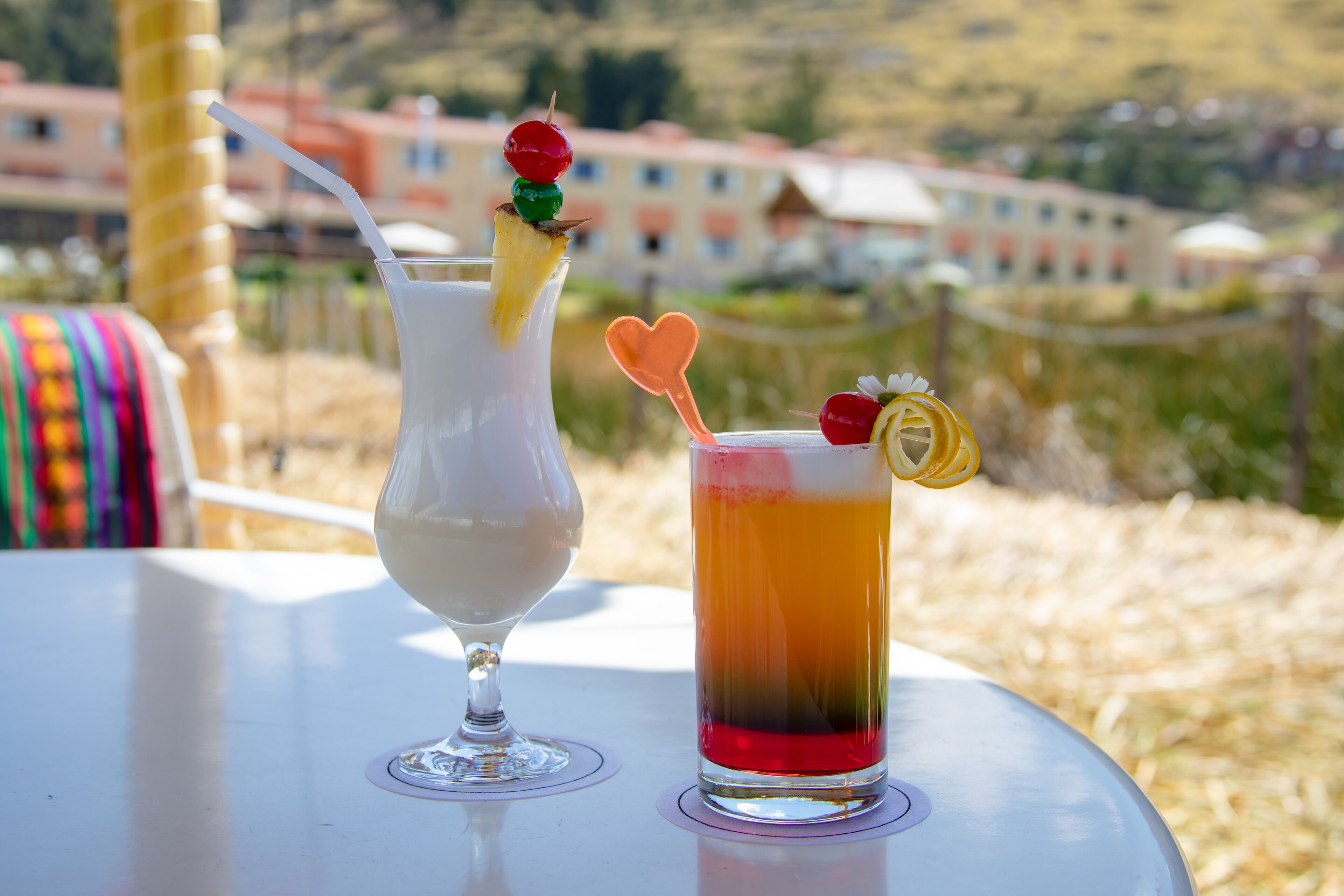 Dos bebidas sobre una mesa con vistas a edificios al fondo.