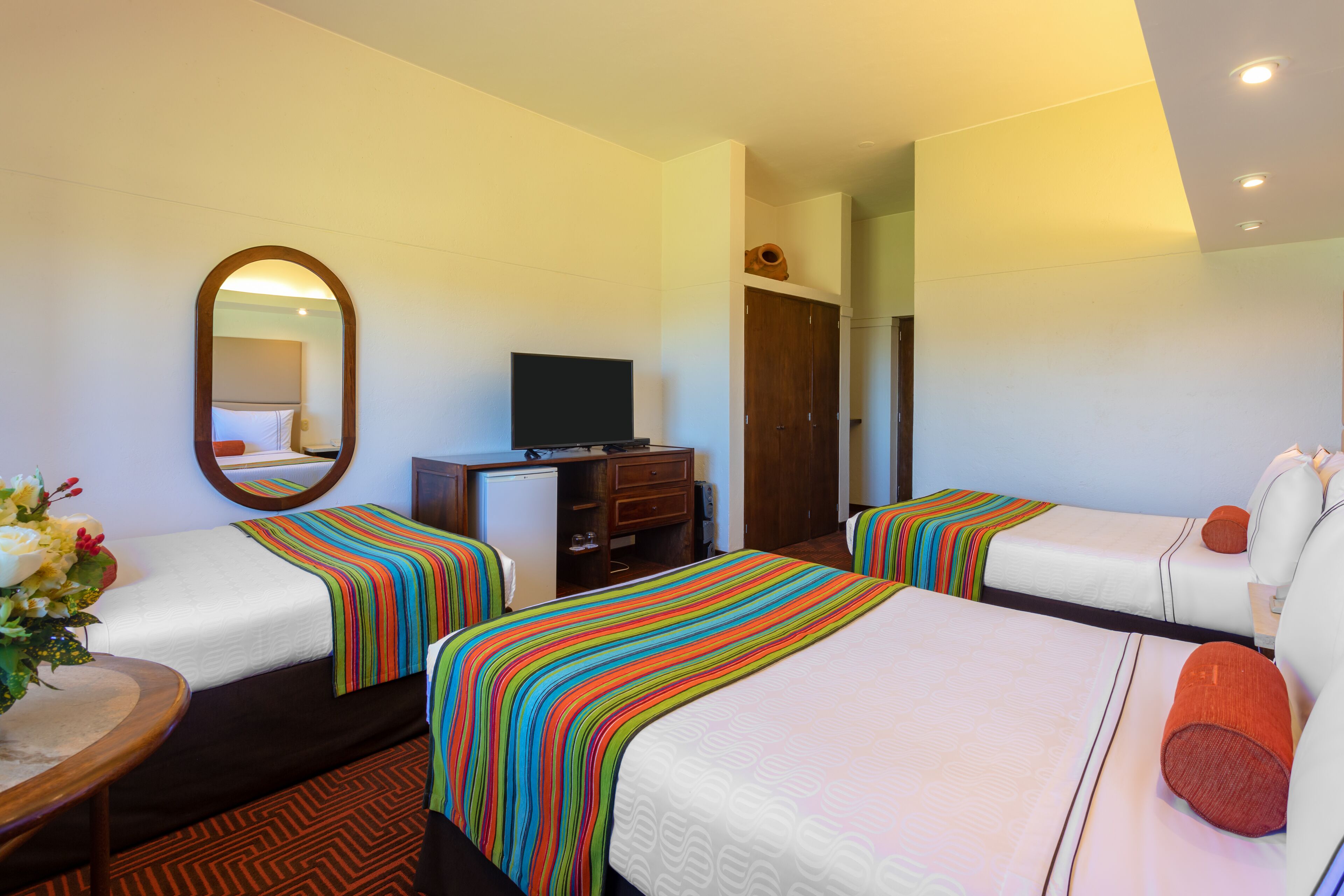 A hotel room with two beds, a TV, a desk, and a mirror.