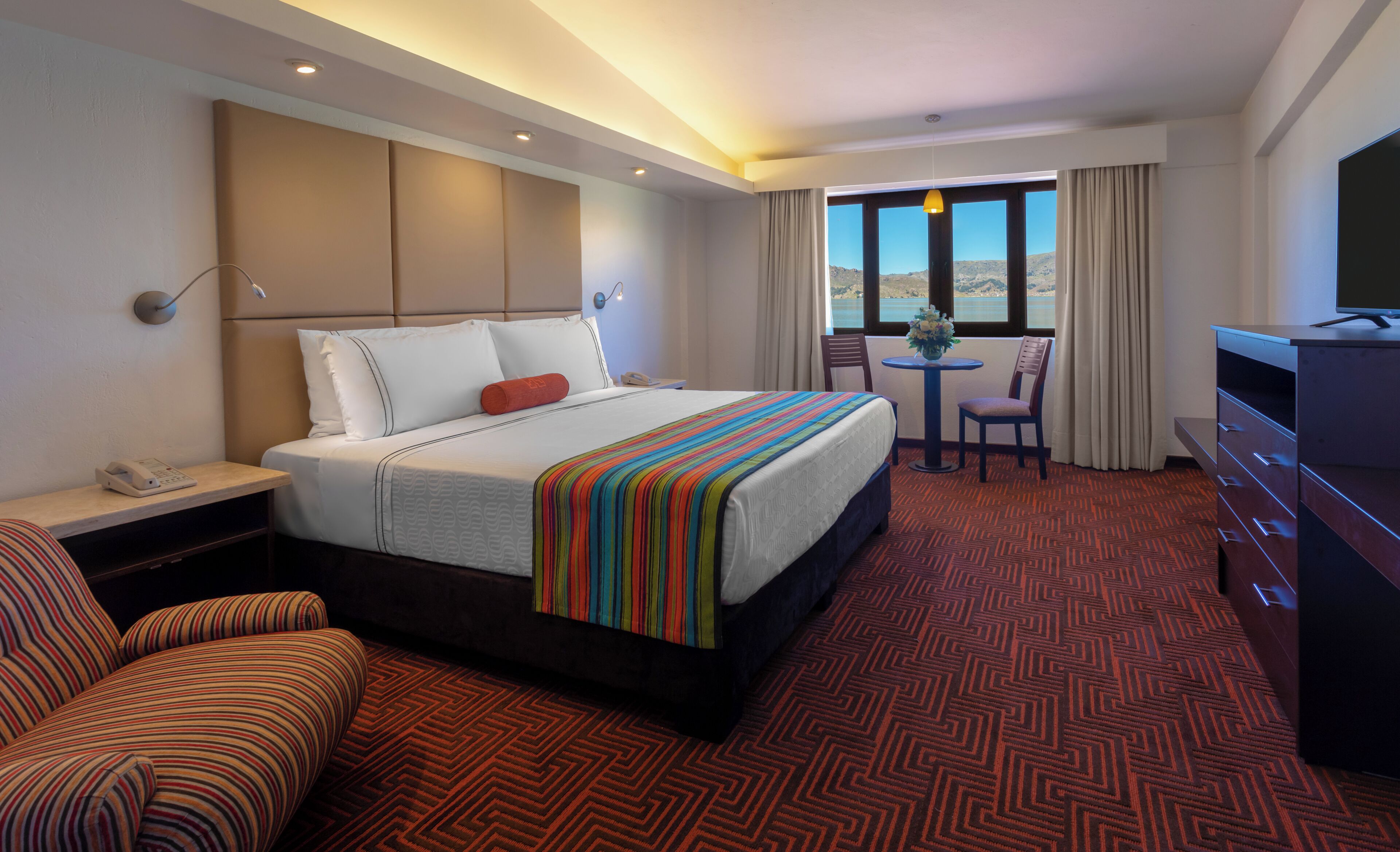 Ein Hotelzimmer mit Bett, Schreibtisch, Stuhl, Fernseher und Blick ins Freie.