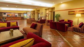 Eine Hotelhalle mit roten Sofas, gestreiften Sesseln, einem Couchtisch und einem Kamin.