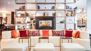 A modern living room with a white sofa, colorful cushions, a fireplace, and a bookshelf filled with books and decorative items. - Hotel Bristol (Geneva)