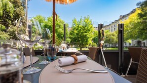 An outdoor dining area with tables set for two, featuring clear glassware and a thatched umbrella. - Hotel Bristol (Geneva)