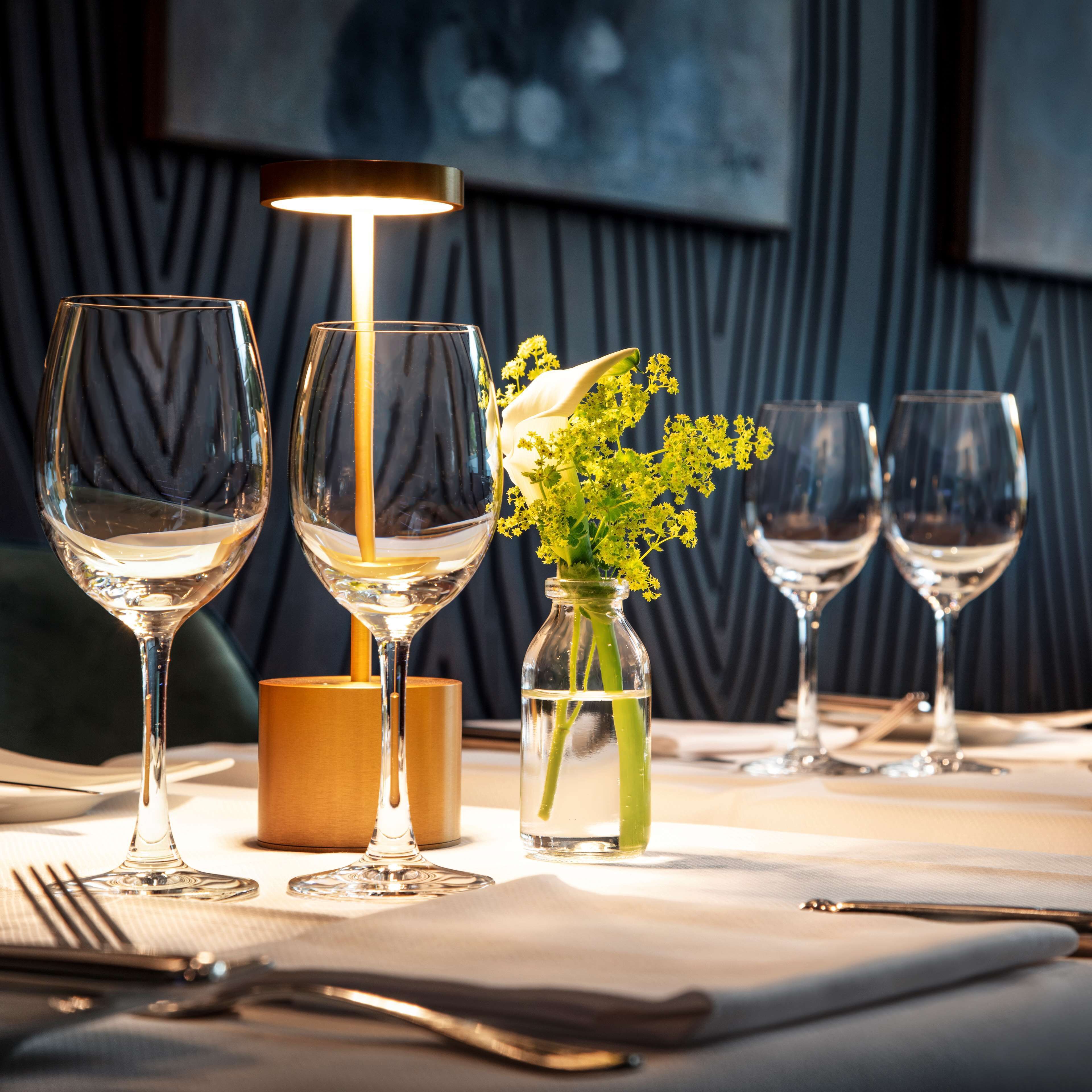 A table set with wine glasses, a candle, and a vase with flowers.