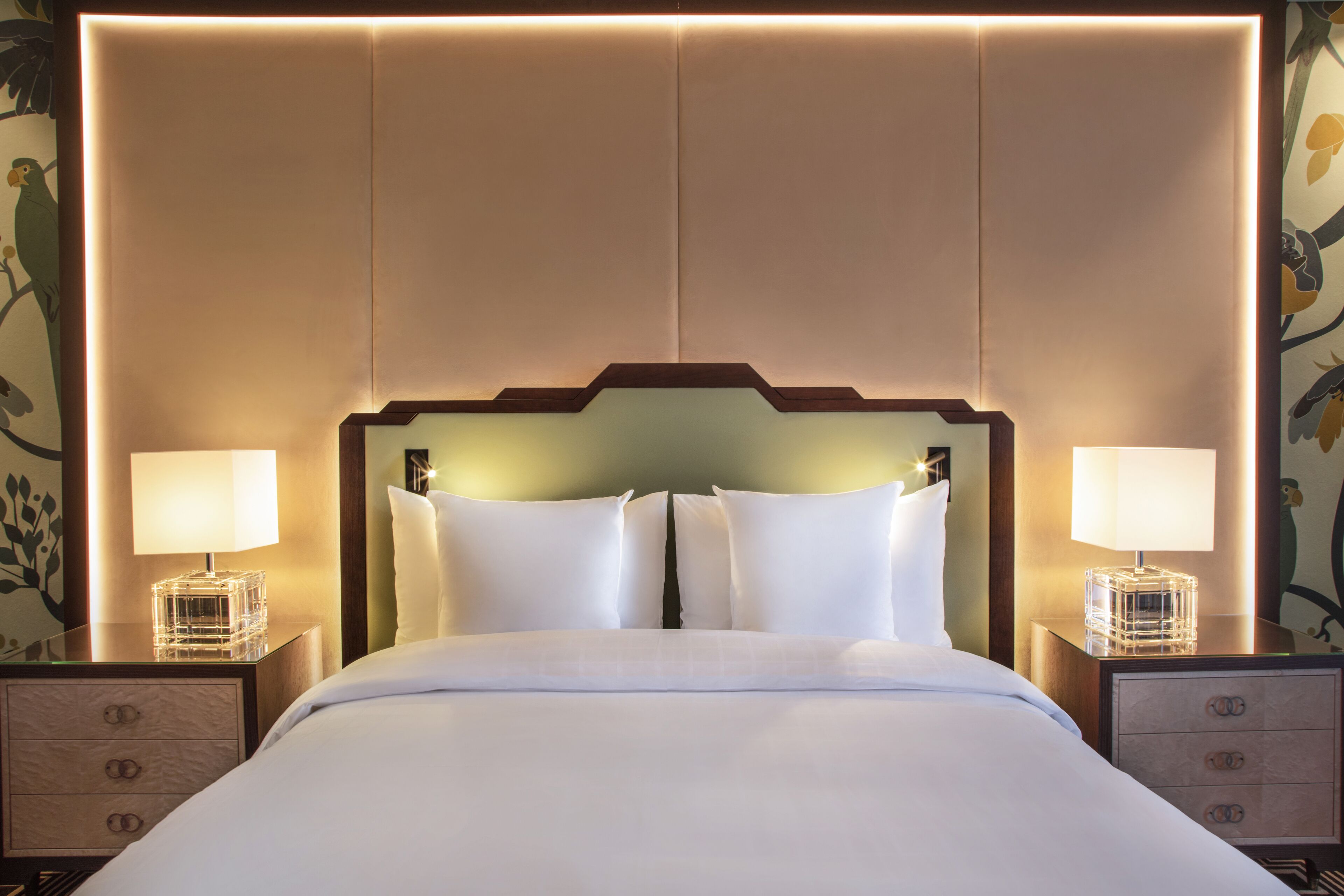 Een hotelkamer met een groot bed, twee nachtkastjes met lampen en een hoofdeinde met ingebouwde verlichting.