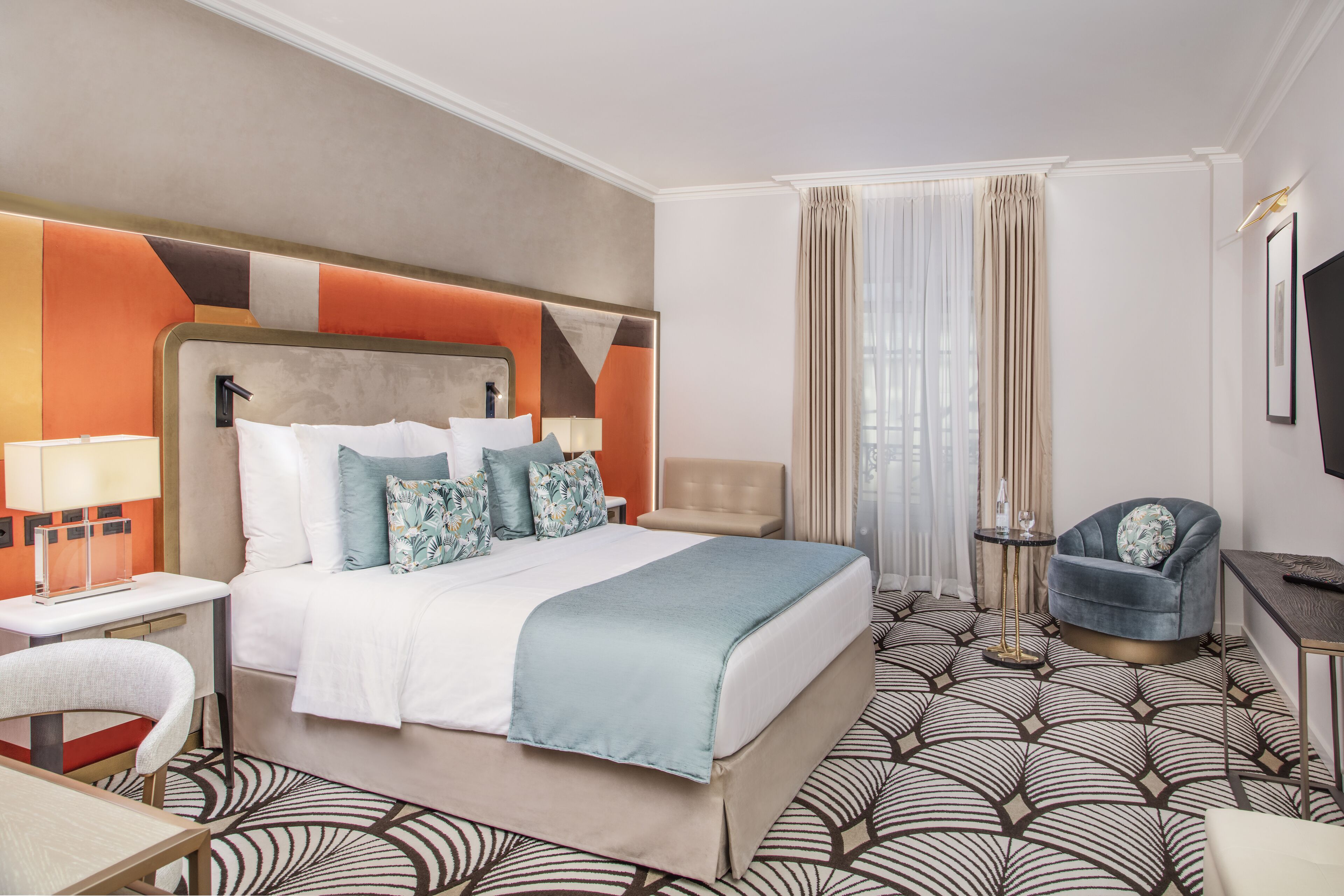 A hotel room with a large bed, a desk, a chair, and a TV.