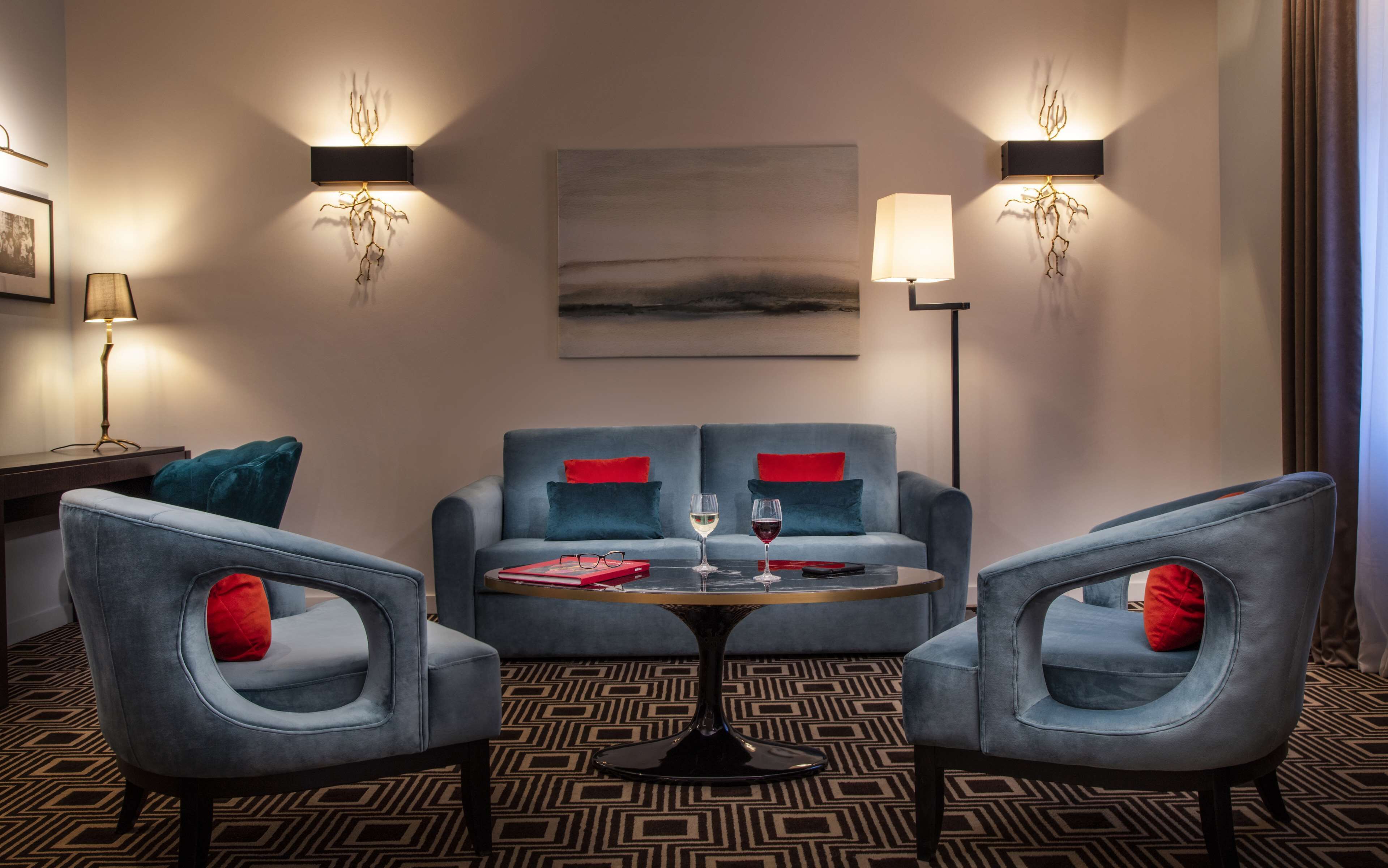 Una habitación de hotel moderna con un conjunto de sofá, dos sillones, una mesita de centro y dos lámparas de pared.