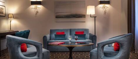 Una habitación de hotel moderna con un conjunto de sofá, dos sillones, una mesita de centro y dos lámparas de pared.