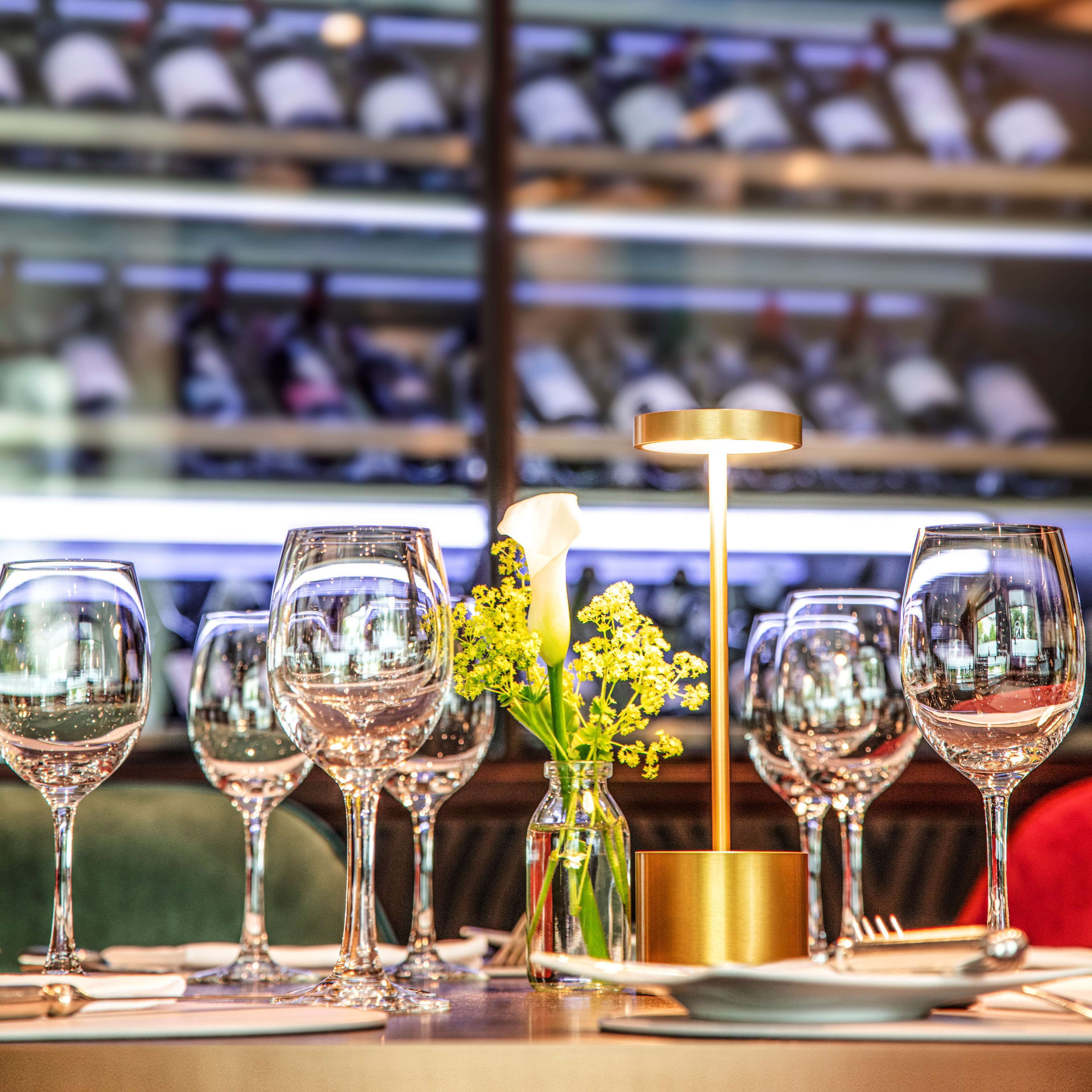A table set with wine glasses, a vase with flowers, and a candle holder.