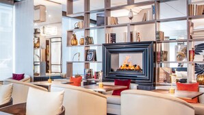 A modern lounge area with leather sofas, a fireplace, and a bookshelf filled with books and decorative items. - Hotel Bristol (Geneva)