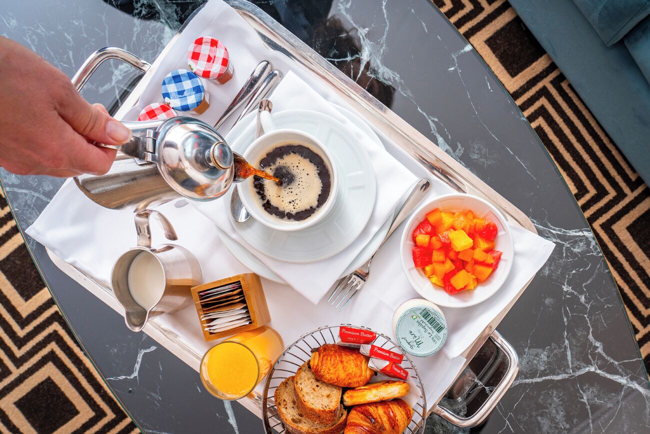 A breakfast tray with a cup of coffee, croissants, orange juice, and a bowl of fruit on a marble table.