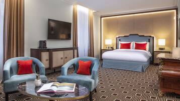 Una habitación de hotel con cama, dos sillones, una mesita de centro, televisión y minibar.