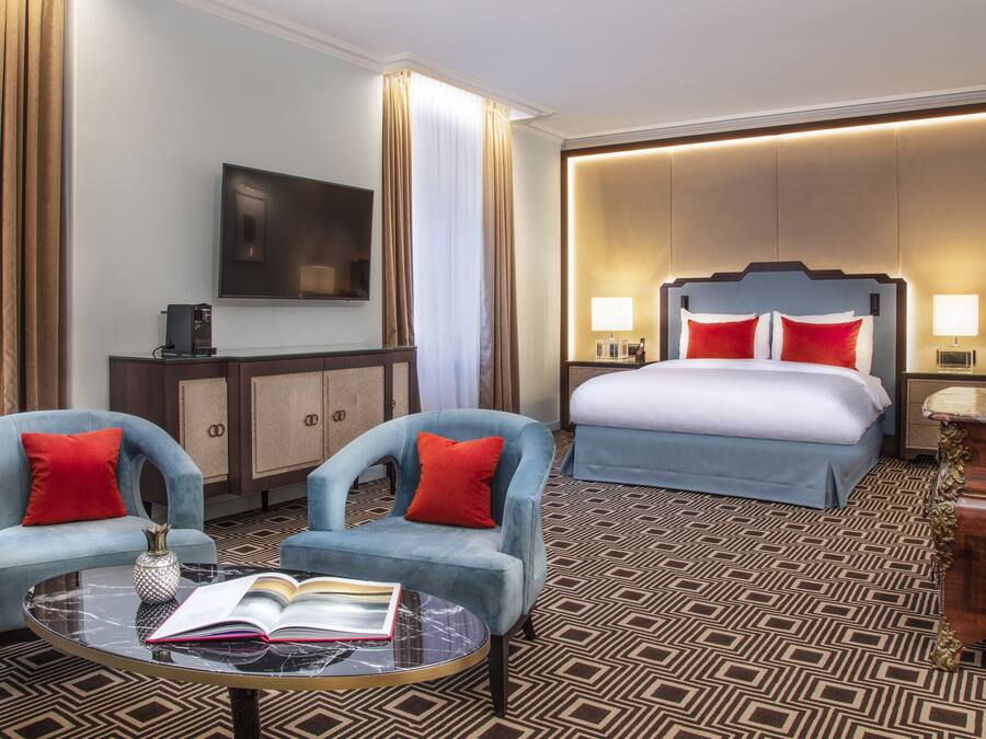 Una habitación de hotel con cama, dos sillones, una mesita de centro, televisión y minibar.