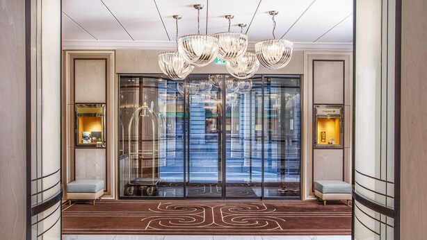 A lobby with a modern chandelier, glass doors, and a marble floor. - Hotel Bristol (Geneva)