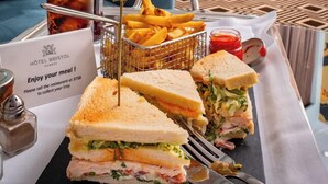 A tray with a sandwich, fries, and a bottle of soda in a hotel room with a view of buildings. - Hotel Bristol (Geneva)