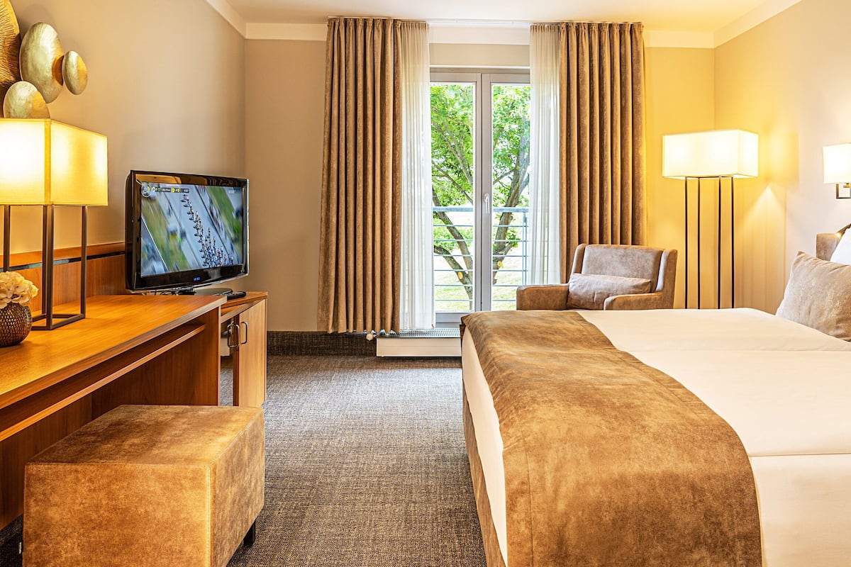 Una habitación de hotel con cama, escritorio con televisor, silla y ventana con cortinas.