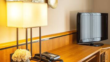 Una habitación de hotel con un escritorio de madera, un teléfono, un televisor y una lámpara.