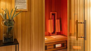 Una sala de sauna con un banco de madera, una puerta de cristal y un florero con plantas sobre una mesa.