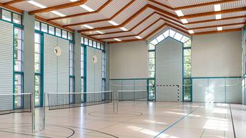 Una cancha de tenis interior con red, vigas de madera y ventanas amplias.
