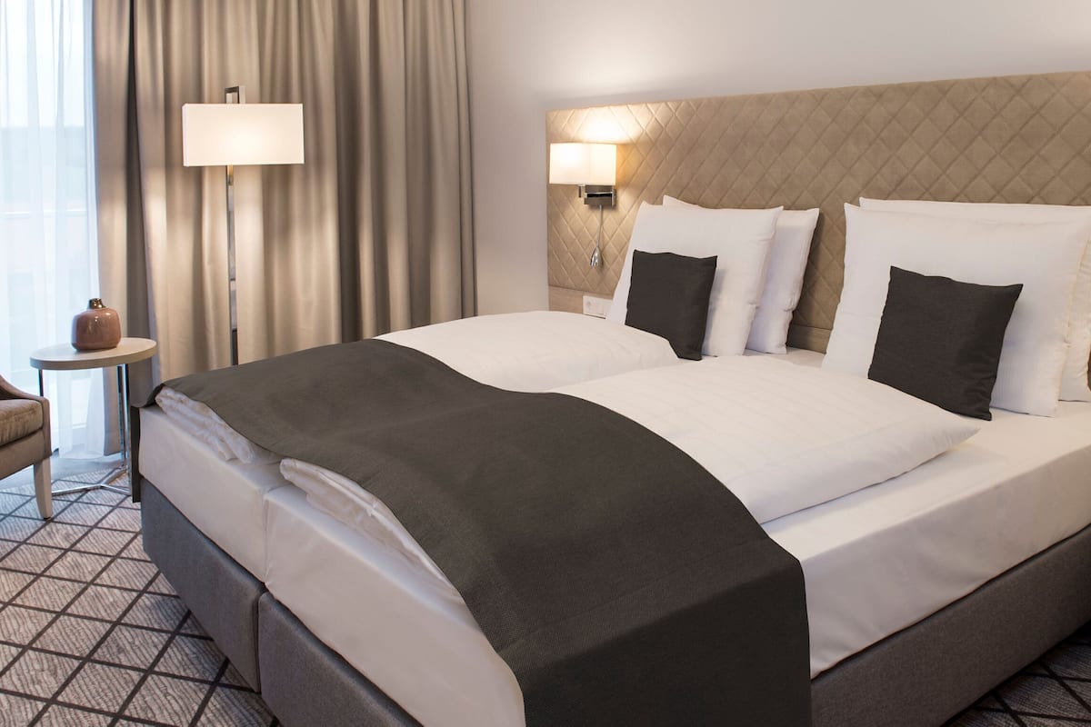 Habitación de hotel con una cama grande, dos mesitas de noche, una lámpara, una silla y vistas al exterior.