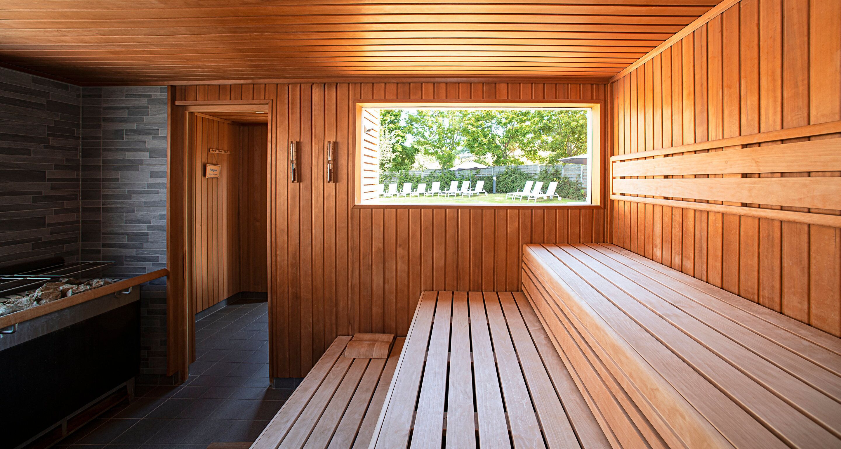 A sauna with wooden benches, a stone wall, and a window overlooking a backyard.