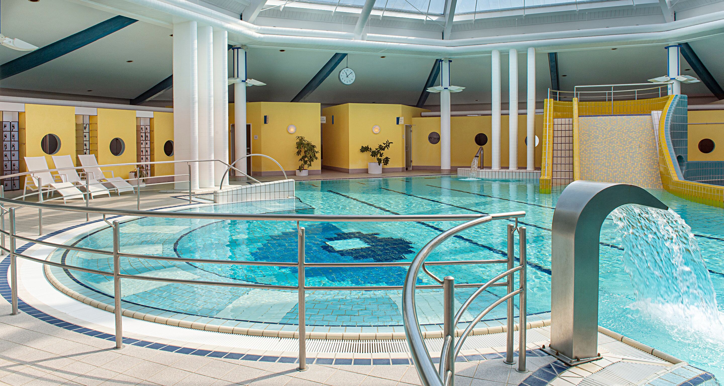 An indoor swimming pool with a circular design, multiple lounge chairs, and a water slide.