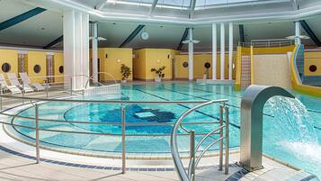 An indoor swimming pool with a circular design, multiple lounge chairs, and a water slide.